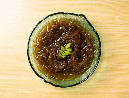 Mozuku placed on a wooden background. View from above.Mozuku is an Okinawan delicacy. It is a kind of dark, thread-like seaweed seasoned with vinegarの写真素材