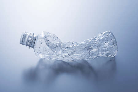 A crushed plastic bottle on a gray background. Concept of recycling and ecology.の写真素材