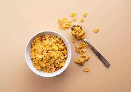 Cornflakes in a bowl and a spoon on a beige background. View from directly above.