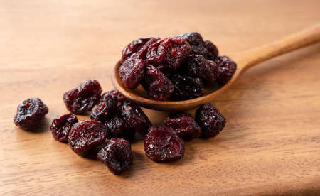 Sweet dried cranberries with a wooden spoon on a wooden background.