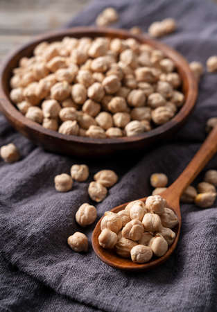 Dried chickpeas in a wooden dish set against an old wooden background, a wooden spoon beside it. Image of chickpeas.の写真素材