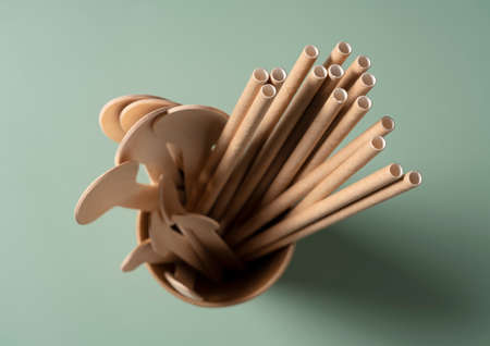 Straws and spoons in disposable paper cups set against a pastel green background. The zero-waste concept. View from above.の写真素材