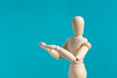 Wooden mannequin with pills on blue background.  Concept of pharmaceuticals and supplements.