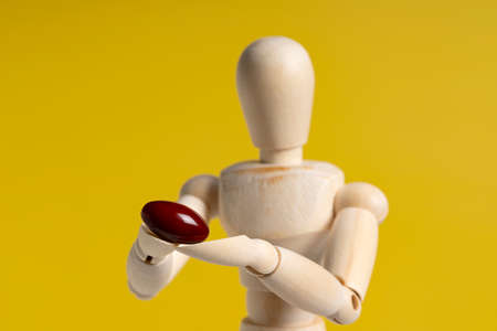 Wooden manikin with pills on yellow background. Concept of pharmaceuticals and supplements.の写真素材