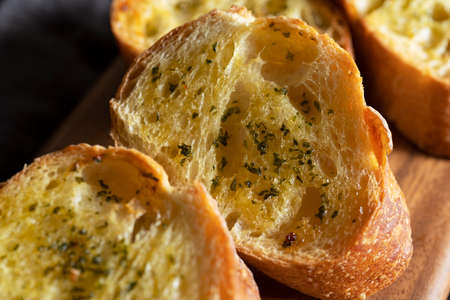 Sliced baked bread with garlic and herbs on a wooden cutting board on the table. Close-up.