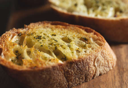 Sliced baked bread with garlic and herbs on a wooden cutting board on the table. Close-up.