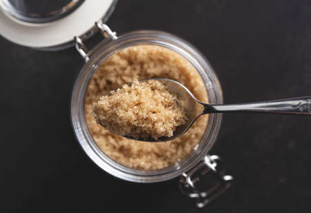 Spooning brown sugar into a glass container set against a black stone background. View from directly above.の写真素材