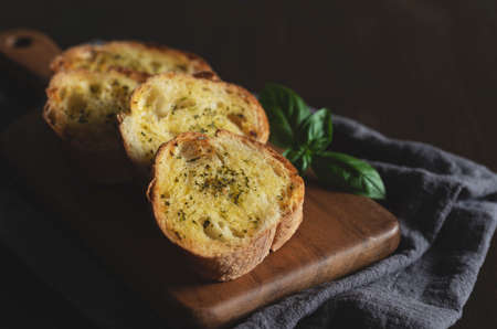 Sliced grilled bread with garlic and herbs on a wooden cutting board on the table. Text space.