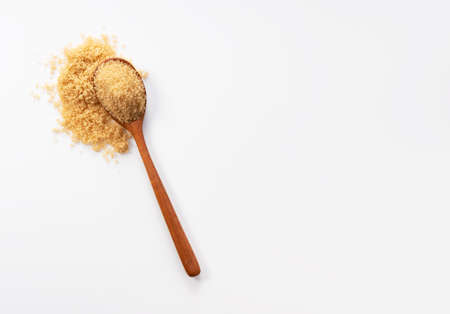 Wooden spoon and brown sugar placed on a white background. View from directly above.