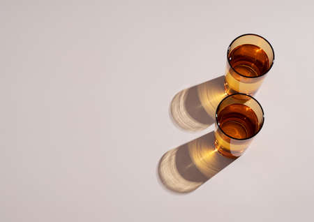 Decorative still life scene in summer. Amber glass with water, long harsh shadows in sunlight. Beige...
