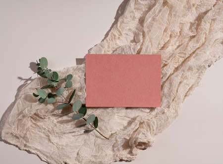 Summer wedding stationery mockup. Plain, orange greeting card, invitation, eucalyptus leaves and gauze fabric on beige background. Natural light and shadow overlay. Flat lay, top view.の写真素材