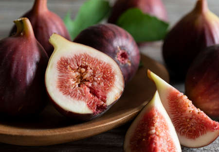 Lots of figs and cut figs on a plate set against a wooden background.