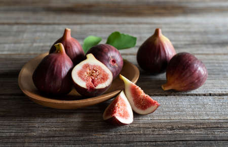 Lots of figs and cut figs on a plate set against a wooden background.