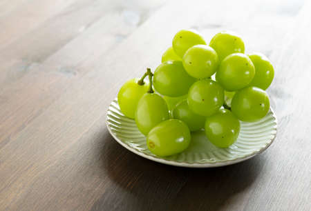 Shine Muscat grapes served on a plate set against a wooden background. White grapes. Japanese grapes.の写真素材