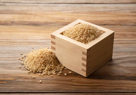 Brown rice in a wooden box set against a wooden background.  A pile of brown rice.の写真素材