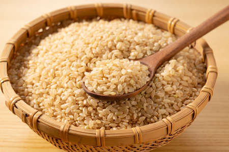 Brown rice in a bamboo colander and a wooden spoon on a wooden background. A pile of brown rice.の写真素材
