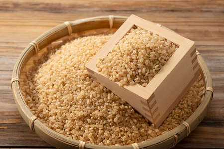 Brown rice in a wooden box and bamboo colander placed on a wooden background.の写真素材