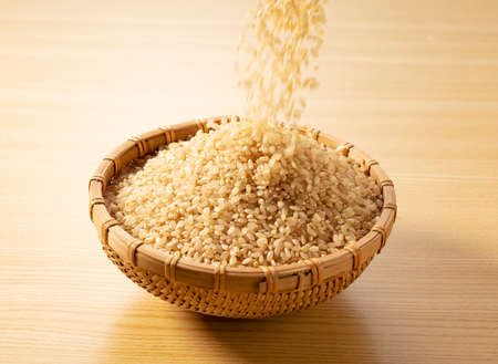 The moment brown rice is poured into a bamboo colander placed on a wooden background.の写真素材