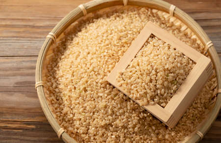 Brown rice in a wooden box and bamboo colander placed on a wooden background.の写真素材