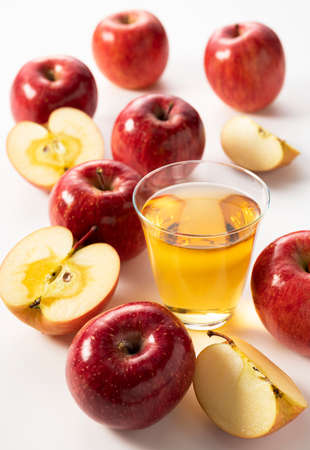Apple juice in a glass cup on a white background with many apples around it.の写真素材