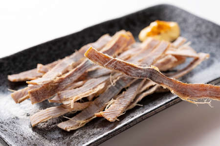Dried squid and mayonnaise on a plate placed on a white background. Surume is a Japanese snack.