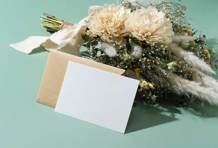 Dried flower bouquet and blank message card placed on green background. Wedding and celebration...