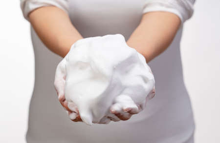 Female holding soap bubbles on white background. Hands with white bubbles. Texture of white soap foam on female hand.の写真素材