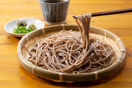 Zaru-soba and condiments on a wooden table. Take soba noodles with chopsticks. Zaru Soba is a traditional Japanese food.の写真素材