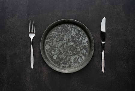 Silver knives and forks on a black background, empty iron plates. Antique, retro. View from above.の写真素材