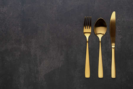 Gold knives, forks and spoons placed on a black background. Beautiful gold cutlery. View from above.の写真素材