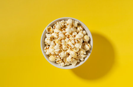Popcorn in a white bowl placed on a yellow background. View from above.