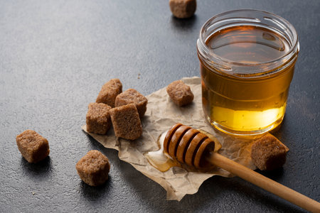 Brown sugar with honey and wooden honey dipper on stone background. Image of beauty.の写真素材