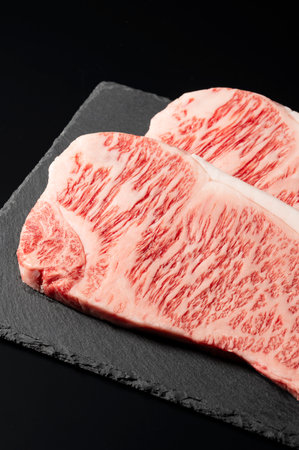 Fresh raw beef steak placed on a stone plate against a black background. Wagyu beef steak.の写真素材