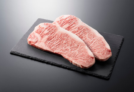 Fresh raw beef steak placed on a stone plate against a black background. Wagyu beef steak.の写真素材