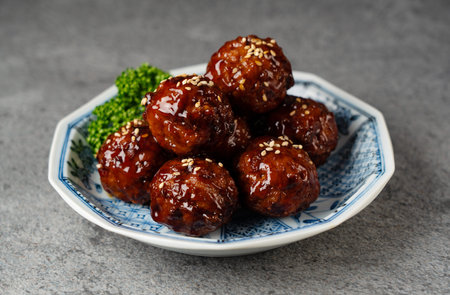 Close-up of Tasty Teriyaki Meatballs with Lettuce on a Patterned Japanese Plate, with Copy Space on Grey Stone Background