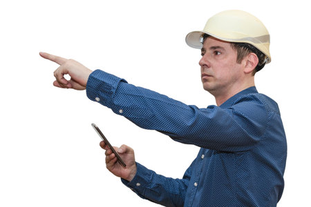 A man in a construction helmet on a white isolated background with with a phone points his hand into the distance. The foreman. Builder. Engineerの写真素材
