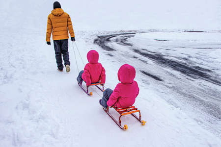 The father drove two twin girls on a sled. Girls in identical twins clothes. Father walks with...