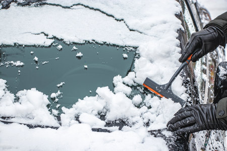 A man is brushing snow from his car. Difficult winter weather conditions for driving a car. Travel...