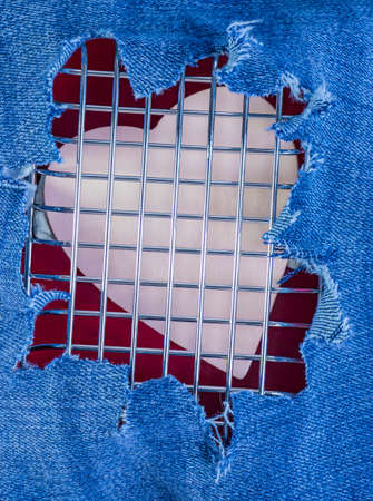 Heart behind a metal grill against the background of torn denim trousers. Love and romance. Complex relationships. Valentine's Day card.の写真素材