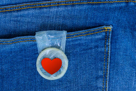 Condom with a red heart hanging from a jeans pocket. Love and romance. Safe sex. Valentine's Day card.の写真素材