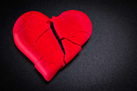 Broken and broken red heart on a black background. Closeup. Vignette. Valentine's Day.の写真素材
