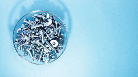 Bolts nuts and washers of different sizes in a glass bowl on a blue background. Concept for advertising construction.の写真素材