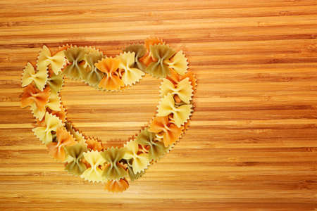 A heart made of multi-colored pasta on a wooden bamboo board.の写真素材