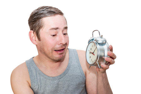 The man was late for work in the morning. Holds a classic alarm clock in his hands. Funny facial expression. Isolated white backgroundの写真素材