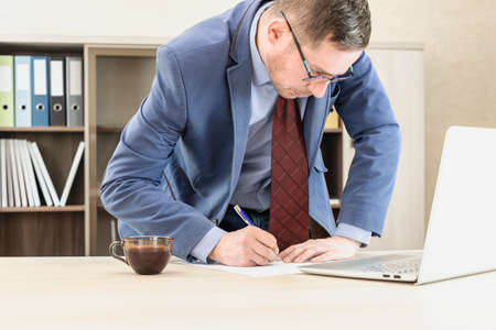 Boss businessman standing near the table signs documents. Strenuous office work. Office worker in...