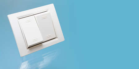White double electrical switch with reflection on a blue background. Close-up. Electrical and...