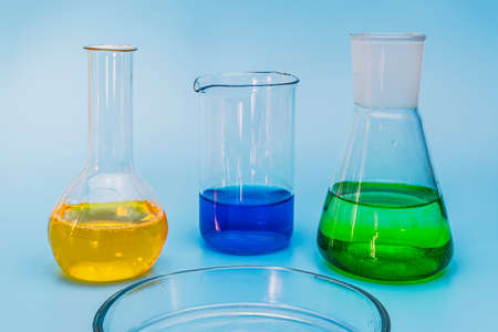 Three glass laboratory flasks with solutions of yellow, green and blue on a gentle blue medical background. The concept of medical and chemical experiments and research. Close-up. copy spaceの写真素材