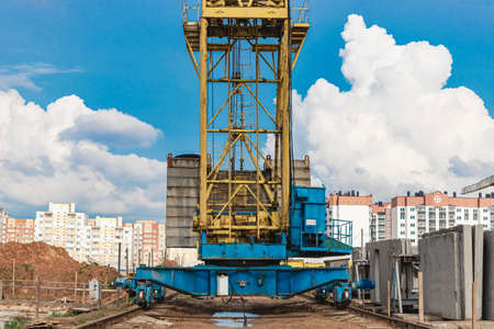 Tower crane on rails close-up at the construction site against the background of the cloudy sky....