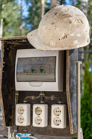 A switchboard on a construction site with sockets and an old work helmet hanging from it. Providing...