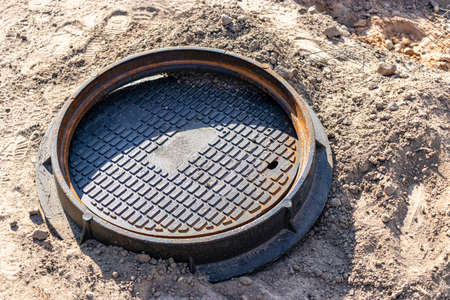A cast-iron sewer manhole prepared for installation. Close-up. Road works. Shelter for underground...